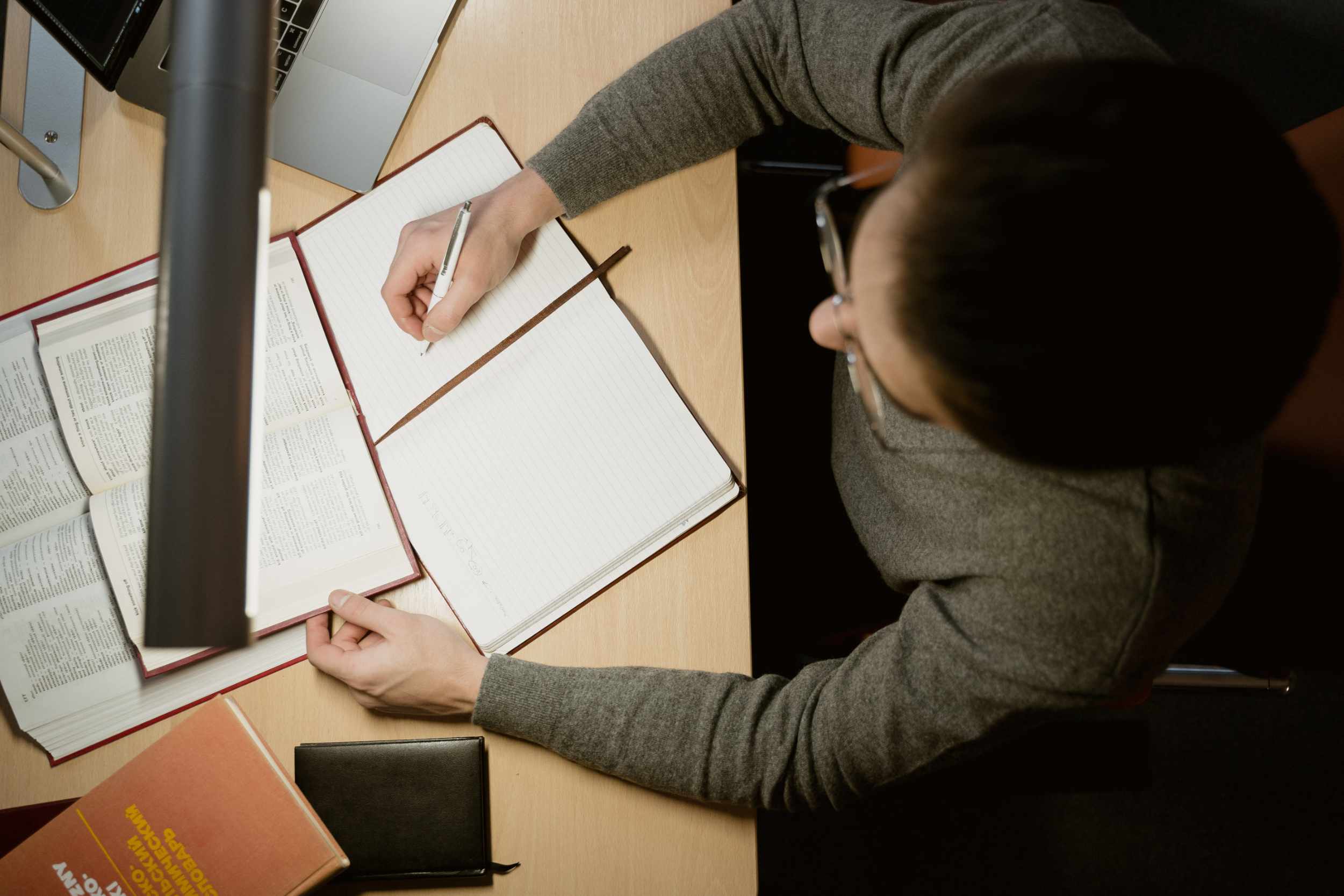 Un uomo, inquadrato dall'alto, scrive su un quaderno con di fronte un libro.